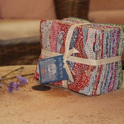 Pacote de tecidos coloridos estampados sobre mesa de pedra, com flores secas e cadeira de vime ao fundo