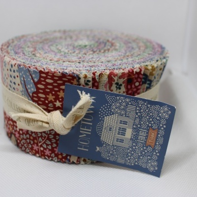 Rolo de tecidos coloridos com padrão floral e geométrico, etiqueta azul com casa desenhada.