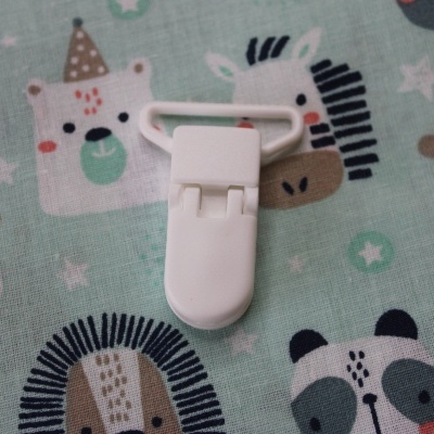 Clipe branco sobre pano com padrão de animais em azul e castanho