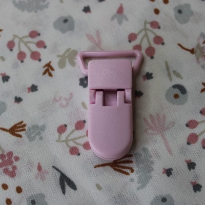 Prendedor de plástico cor-de-rosa sobre tecido com padrão floral colorido