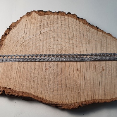 Laço cinza estreito com franjas sobre fatia de madeira com casca