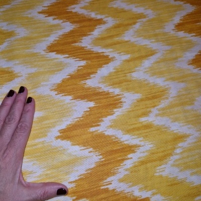 Tecido amarelo, branco e castanho com padrão abstrato, mão para escala