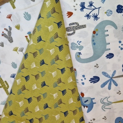 Três tecidos com padrões coloridos de dinossauros, cactos e folhas em branco e verde