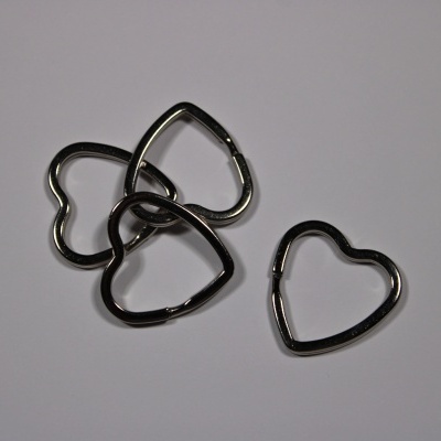 Argolas metálicas prateadas em forma de coração sobre superfície cinzenta.