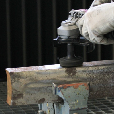 Rebolo elétrico cinzento a polir barra de metal enferrujada numa morsa azul