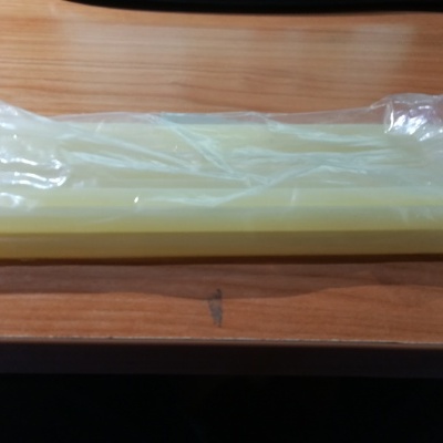 Três bastões de cola quente amarelos em embalagem transparente sobre madeira clara