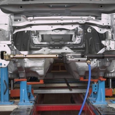 Estrutura metálica branca de carro numa plataforma azul e amarela em oficina.