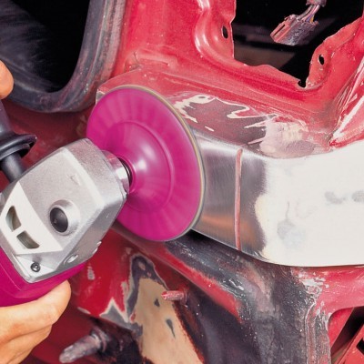 Lixadeira elétrica com disco rosa a lixar metal prateado de carro vermelho.