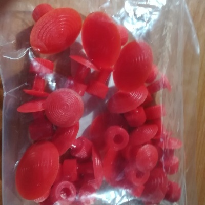 Peças plásticas vermelhas em saco transparente sobre madeira