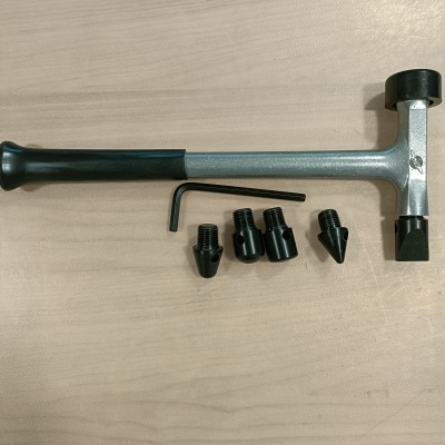 Ferramenta metálica com cabo preto e acessórios pretos numa mesa de madeira