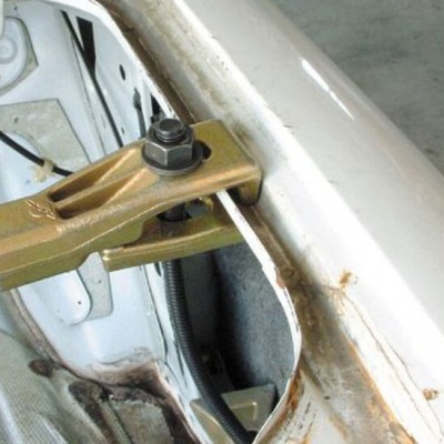 Ferramenta metálica dourada numa estrutura metálica branca com sinais de ferrugem e superfície cinza ao fundo