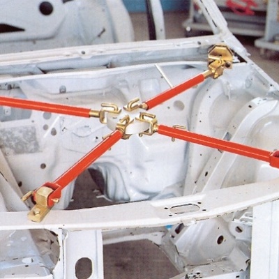 Estrutura metálica branca de carro com varas transversais vermelhas e juntas douradas numa oficina