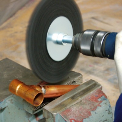 Rebarbadora elétrica com roda abrasiva a funcionar perto de uma peça de metal de cobre numa morsa azul