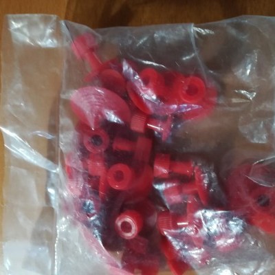 Pacote plástico com rebites ou parafusos vermelhos e porcas em superfície de madeira