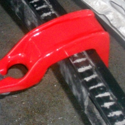 Gancho de reboque vermelho metálico com corrente e superfície preta riscada ao fundo