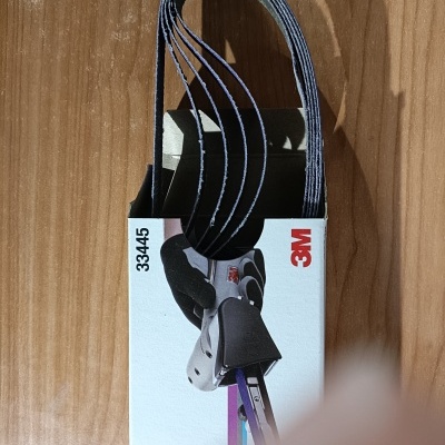 Correias abrasivas pretas 3M 33445 em embalagem branca sobre mesa de madeira.