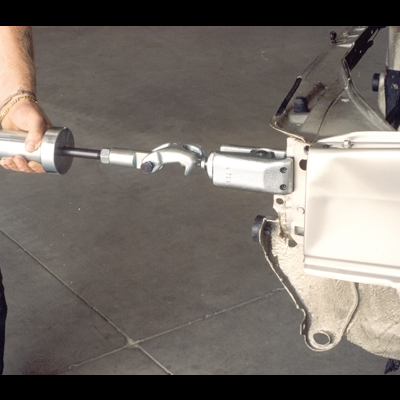 Pessoa com ferramenta metálica junto a componente mecânico branco sobre chão de cimento