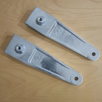 Dois suportes metálicos prateados com orifícios e pinos sobre madeira clara