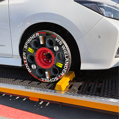 Roda de carro com pneu preto com texto branco e centro vermelho presa num suporte amarelo.