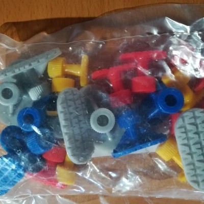 Pacote com peças de plástico coloridas para montar, sobre uma mesa de madeira.