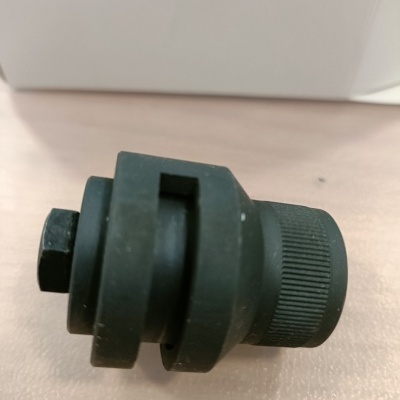 Peça mecânica preta cilíndrica com superfície estriada e formato hexagonal sobre superfície clara