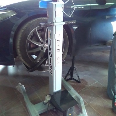 Elevador hidráulico de chão para automóveis com base cinzenta e coluna branca na oficina ao lado de um carro preto