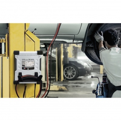 Carregador de bateria CYCLON 12/24 V montado em parede amarela numa oficina com mecânico ao lado