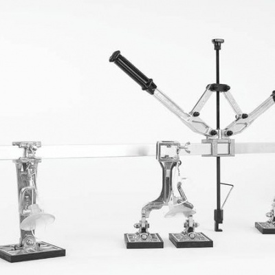 Equipamento metálico articulado com suporte em bases pretas num fundo branco.