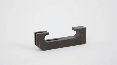 Peça metálica preta com formato retangular e recortes em fundo branco