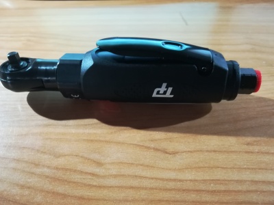 Chave de catraca pneumática preta com botão vermelho sobre madeira