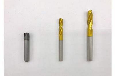 Três brocas metálicas em fundo branco, duas com ponta dourada e uma cinza.