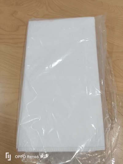 Toalha ou tecido branco embalado em plástico sobre mesa de madeira.