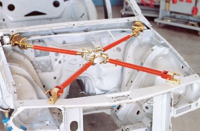 Estrutura metálica branca de carro com varas transversais vermelhas e juntas douradas numa oficina