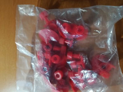 Pacote plástico com rebites ou parafusos vermelhos e porcas em superfície de madeira