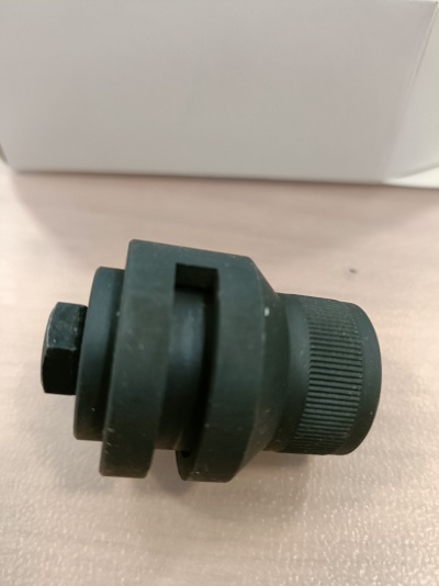 Peça mecânica preta cilíndrica com superfície estriada e formato hexagonal sobre superfície clara