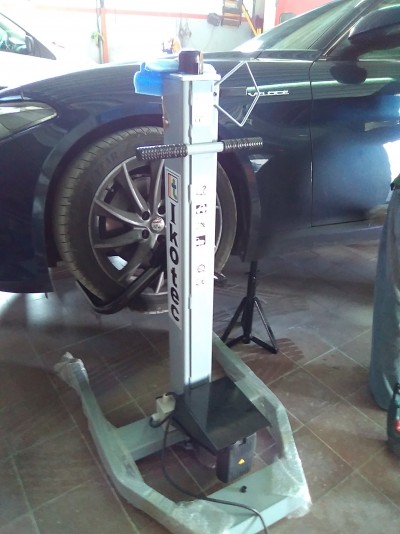 Elevador hidráulico de chão para automóveis com base cinzenta e coluna branca na oficina ao lado de um carro preto