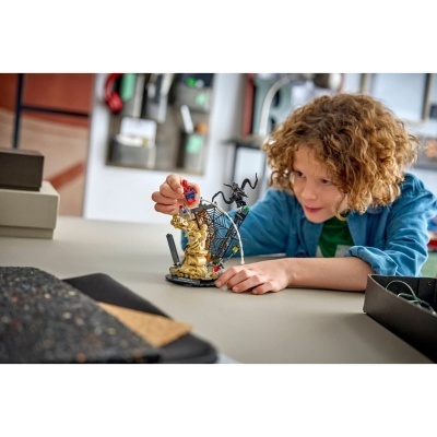 Menino brinca com figuras LEGO Spider-Man sobre mesa cinza num interior