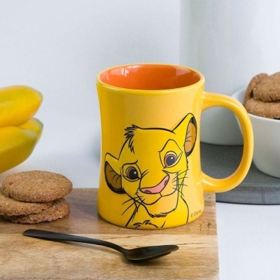 Caneca amarela com estampa do Simba da Disney em bancada de madeira com biscoitos e colher