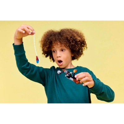 Criança segura brinquedos LEGO Homem-Aranha e mota de fogo em fundo amarelo