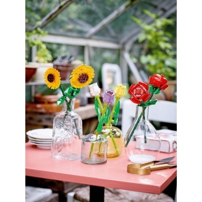 Flores de LEGO coloridas em vasos de vidro numa mesa cor de rosa