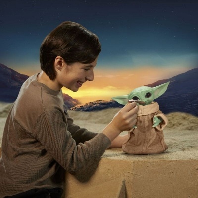 Boneco Baby Yoda em roupas castanhas com pessoa e paisagem ao fundo