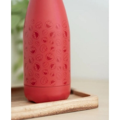 Garrafa vermelha com padrão de carinhas sorridentes na bandeja de madeira