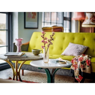 Sala de estar com sofá amarelo, mesas redondas com decoração e janela grande ao fundo