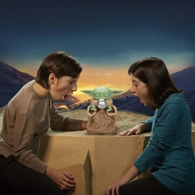 Crianças olhando para figura de Baby Yoda com esfera prateada em cenário montanhoso ao pôr do sol