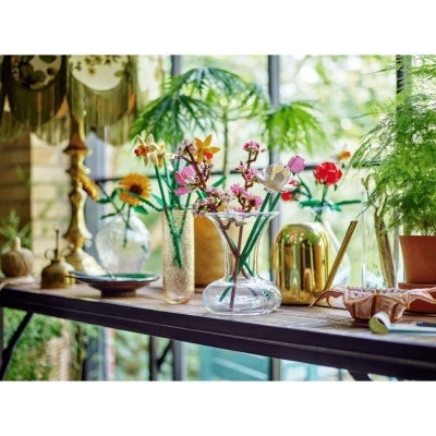 Mesa de madeira com vasos de vidro com flores artificiais e regador dourado numa decoração interior