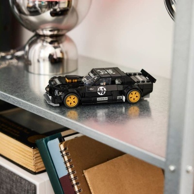 Carrinho preto de brinquedo de construção com rodas amarelas numa prateleira metálica.