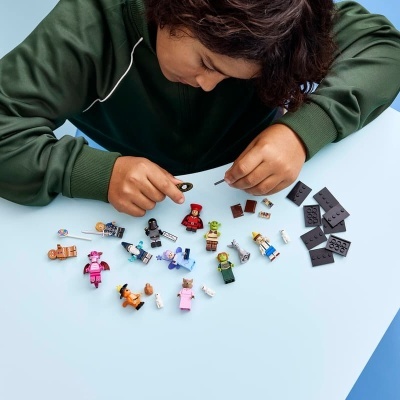 Pessoa a montar minifiguras LEGO diversas sobre mesa azul