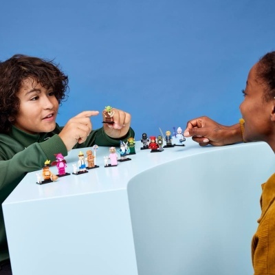 Crianças a brincar com figuras LEGO coloridas sobre superfície branca e fundo azul