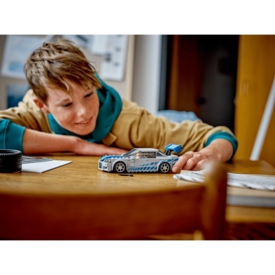 Criança a brincar com carro de blocos de construção azul e cinza numa mesa de madeira