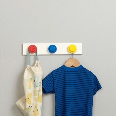 Cabide branco com ganchos vermelho, azul e amarelo, t-shirt azul riscada e mochila bege ilustrada penduradas